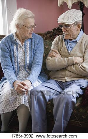 Senior couple conversing while sitting on sofa in living room View Large Photo Image Stock Image - Senior couple conversing while sitting on sofa in living room. Fotosearch