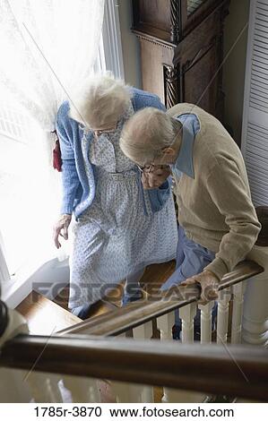 Stock Image - Senior couple helping one another carefully climb up stairs. Fotosearch