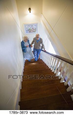 Stock Image - Senior couple helping one another carefully climb up stairs. Fotosearch