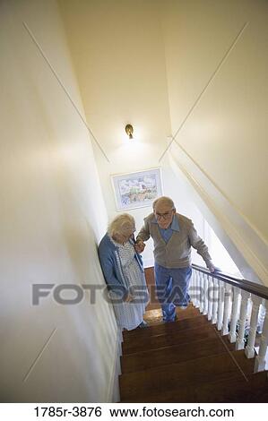 Stock Photograph - Senior couple helping one another carefully climb up stairs. Fotosearch