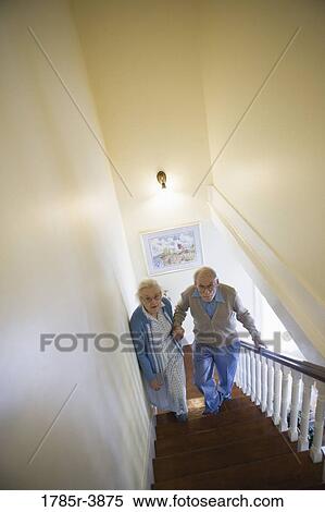 Stock Photography - Senior couple helping one another carefully climb up stairs. Fotosearch