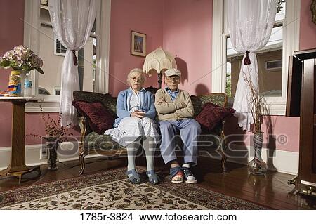 Picture - Senior couple sitting on sofa in living room. Fotosearch