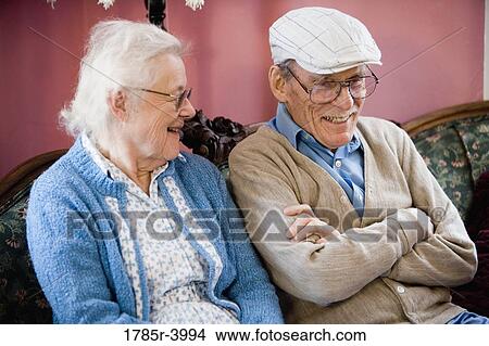 Senior couple smiling while sitting on sofa in living room View Large Photo Image Picture - Senior couple smiling while sitting on sofa in living room. Fotosearch