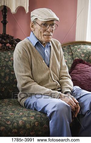 Stock Image - Senior man sitting on a sofa in living room. Fotosearch