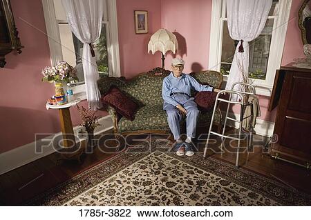 Senior man sitting on sofa in living room View Large Photo Image Stock Image - Senior man sitting on sofa in living room. Fotosearch