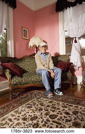 Senior man sitting on sofa in living room View Large Photo Image Stock Image - Senior man sitting on sofa in living room. Fotosearch