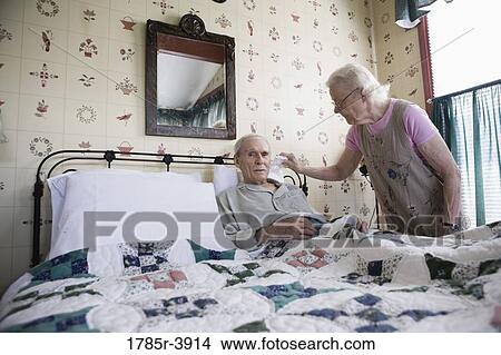Senior woman affectionately tending to bedridden senior man View Large Photo Image Picture - Senior woman affectionately tending to bedridden senior man. Fotosearch