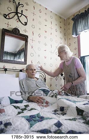 Stock Photography - Senior woman affectionately tending to bedridden senior man. Fotosearch