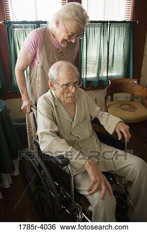 Stock Photograph - Senior woman helping senior man in a wheelchair. Fotosearch