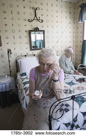 Senior woman sitting on bed looking at prescription bottle View Large Photo Image Stock Image - Senior woman sitting on bed looking at prescription bottle. Fotosearch