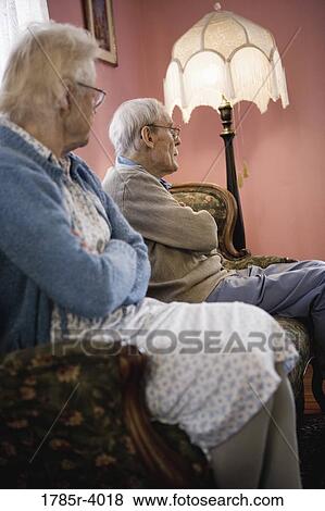 Senior woman sitting on sofa being ignored by senior man View Large Photo Image Stock Photo - Senior woman sitting on sofa being ignored by senior man. Fotosearch
