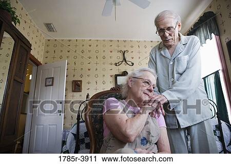 Stock Image - Senior woman sitting with senior man's hand resting on her shoulder. Fotosearch