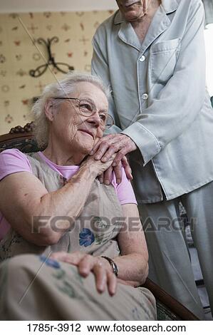 Stock Image - Senior woman sitting with senior man's hand resting on her shoulder. Fotosearch