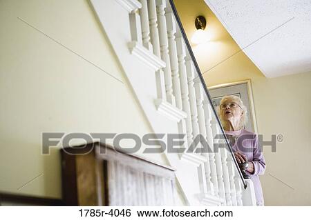Senior woman standing by staircase alone, looking up the stairs View Large Photo Image Stock Photograph - Senior woman standing by staircase alone, looking up the stairs. Fotosearch