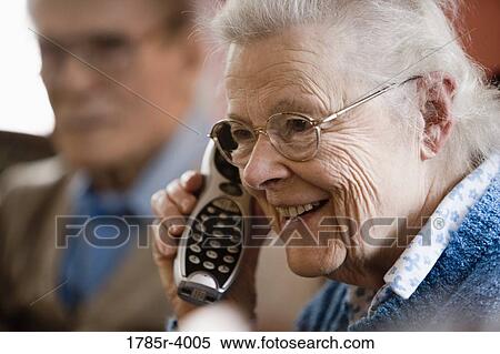 Senior woman talking on cordless phone with senior man in background View Large Photo Image Stock Photography - Senior woman talking on cordless phone with senior man in background. Fotosearch