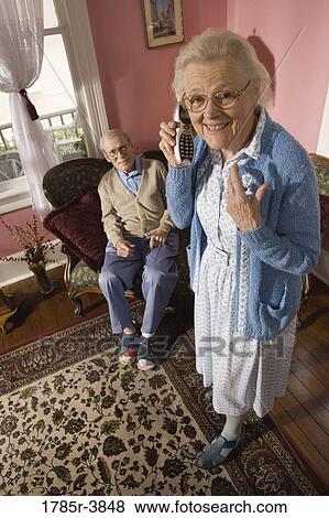 Senior woman talks on cordless phone while grumpy senior man watches View Large Photo Image Stock Photo - Senior woman talks on cordless phone while grumpy senior man watches. Fotosearch