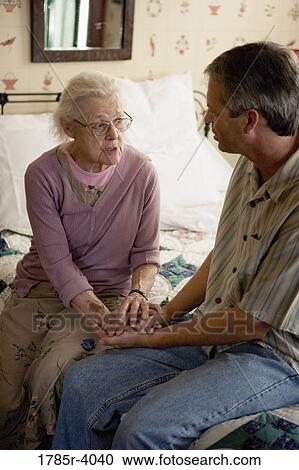 Senior woman with adult son conversing while sitting on bed View Large Photo Image Stock Image - Senior woman with adult son conversing while sitting on bed. Fotosearch