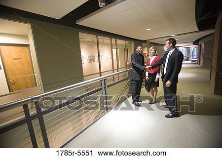 Side view of business people conversing and shaking hands in office corridor View Large Photo Image Stock Image - Side view of business people conversing and shaking hands in office corridor. Fotosearch