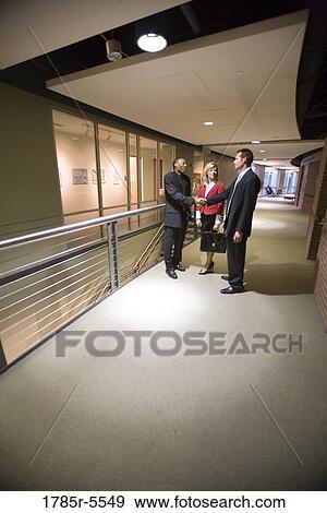 Side view of business people conversing and shaking hands in office corridor View Large Photo Image Stock Photo - Side view of business people conversing and shaking hands in office corridor. Fotosearch