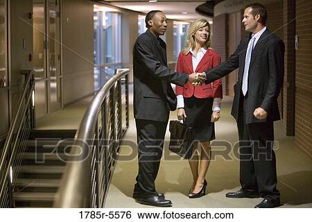Side view of businesspeople standing in an office hallway and lobby shaking hands View Large Photo Image Stock Photograph - Side view of businesspeople standing in an office hallway and lobby shaking hands. Fotosearch