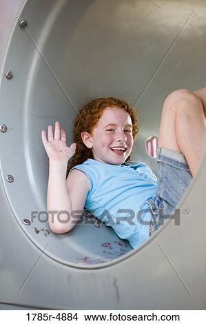 Picture - Smiling girl sitting in a tunnel and waving at a playground. Fotosearch
