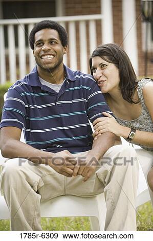 Stock Photo - Smiling young inter-racial couple sitting on lawn chairs in front of house. Fotosearch