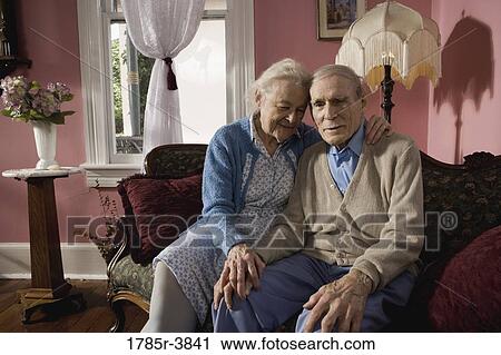 Stock Image - Stoic senior couple sitting on sofa in living room. Fotosearch