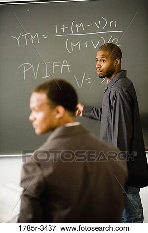 Student writing on the chalkboard in front of teacher View Large Photo Image Stock Photo - Student writing on the chalkboard in front of teacher. Fotosearch