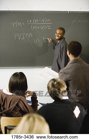 Student writing on the chalkboard in front of classmates and teacher View Large Photo Image Stock Photograph - Student writing on the chalkboard in front of classmates and teacher. Fotosearch
