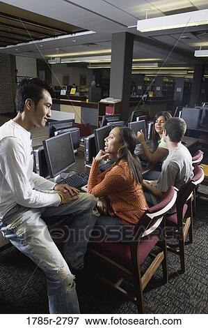 Stock Photo - Students conversing while using computers in the library. Fotosearch