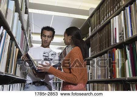 Stock Image - Students in the library looking through book stacks. Fotosearch