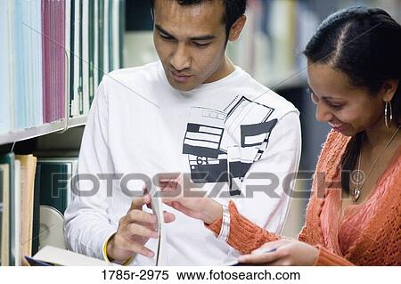 Stock Photography - Students reading a book amidst library book stacks. Fotosearch