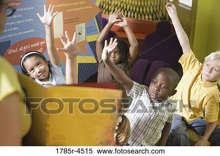 Stock Photography - Students sitting in classroom, raising their hands to their teacher. Fotosearch