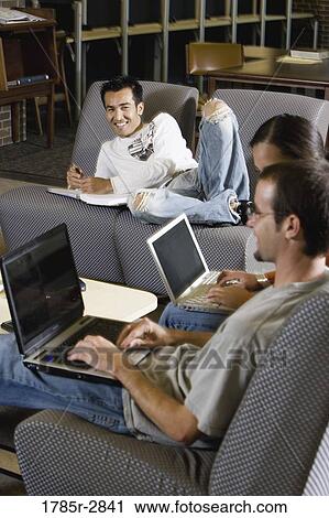 Stock Image - Students with laptop computers in library sitting on sofas studying. Fotosearch