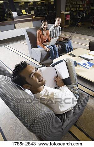 Stock Image - Students with laptop computers in library sitting on sofas studying. Fotosearch