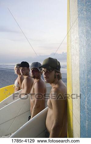 Stock Photo - Surfer dudes and girl posing on beach at sunrise with surfboards. Fotosearch