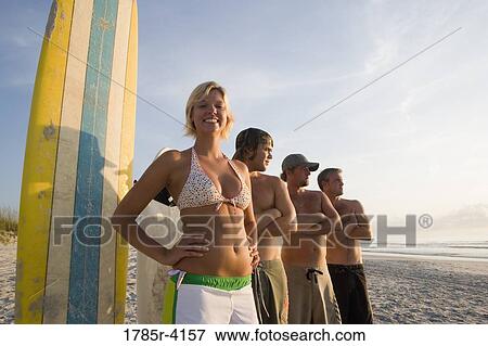 Stock Photo - Surfer dudes and girl posing on beach surfboards. Fotosearch