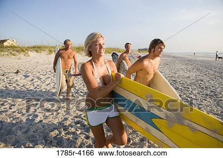 Stock Photograph - Surfer dudes and girl running towards surf with surfboards. Fotosearch