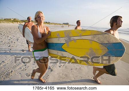 Stock Photography - Surfer dudes and girl running towards surf with surfboards. Fotosearch