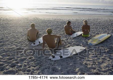Picture - Surfer dudes and girl sitting on beach at sunrise with surfboards. Fotosearch