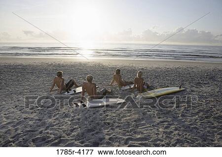 Surfer dudes and girl sitting on beach at sunrise with surfboards View Large Photo Image Stock Photo - Surfer dudes and girl sitting on beach at sunrise with surfboards. Fotosearch