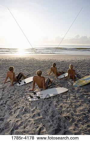 Stock Photo - Surfer dudes and girl sitting on beach at sunrise with surfboards. Fotosearch