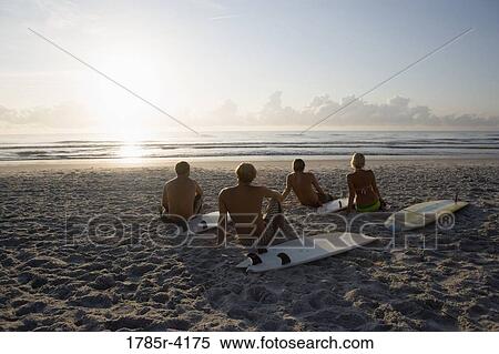 Surfer dudes and girl sitting on beach at sunrise with surfboards View Large Photo Image Stock Photography - Surfer dudes and girl sitting on beach at sunrise with surfboards. Fotosearch