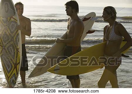 Surfer dudes and girl standing on water's edge at beach with surfboards View Large Photo Image Stock Photo - Surfer dudes and girl standing on water's edge at beach with surfboards. Fotosearch