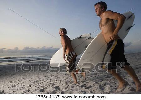 Stock Photo - Surfer dudes running towards surf with surfboards. Fotosearch