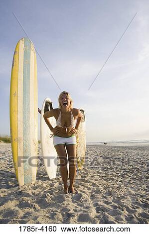 Stock Image - Surfer girl posing on beach with surfboards. Fotosearch