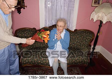 Surprised and happy senior woman sitting on the sofa handed bouquet of flowers View Large Photo Image Stock Photo - Surprised and happy senior woman sitting on the sofa handed bouquet of flowers. Fotosearch