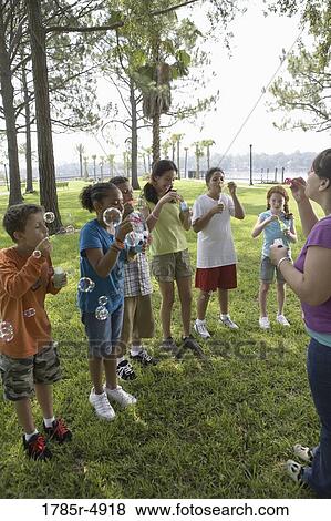 Teacher and children blowing bubbles at a park View Large Photo Image Stock Photo - Teacher and children blowing bubbles at a park. Fotosearch