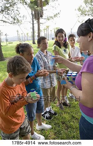 Teacher distributing bubble bottles to children at a park View Large Photo Image Picture - Teacher distributing bubble bottles to children at a park. Fotosearch