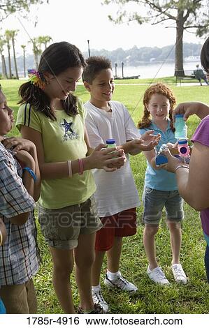 Stock Photograph - Teacher distributing bubble bottles to children at a park. Fotosearch